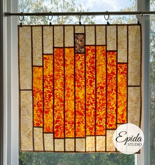 Decorative quilt with autumnal patterns hanging on a rod, featuring the brand 'Epida Studio'.