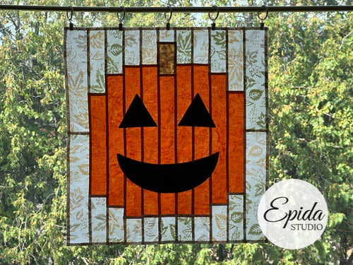 Stained glass pumpkin with a smiling face in front of a forest background, featuring the brand 'Epida Studio'.