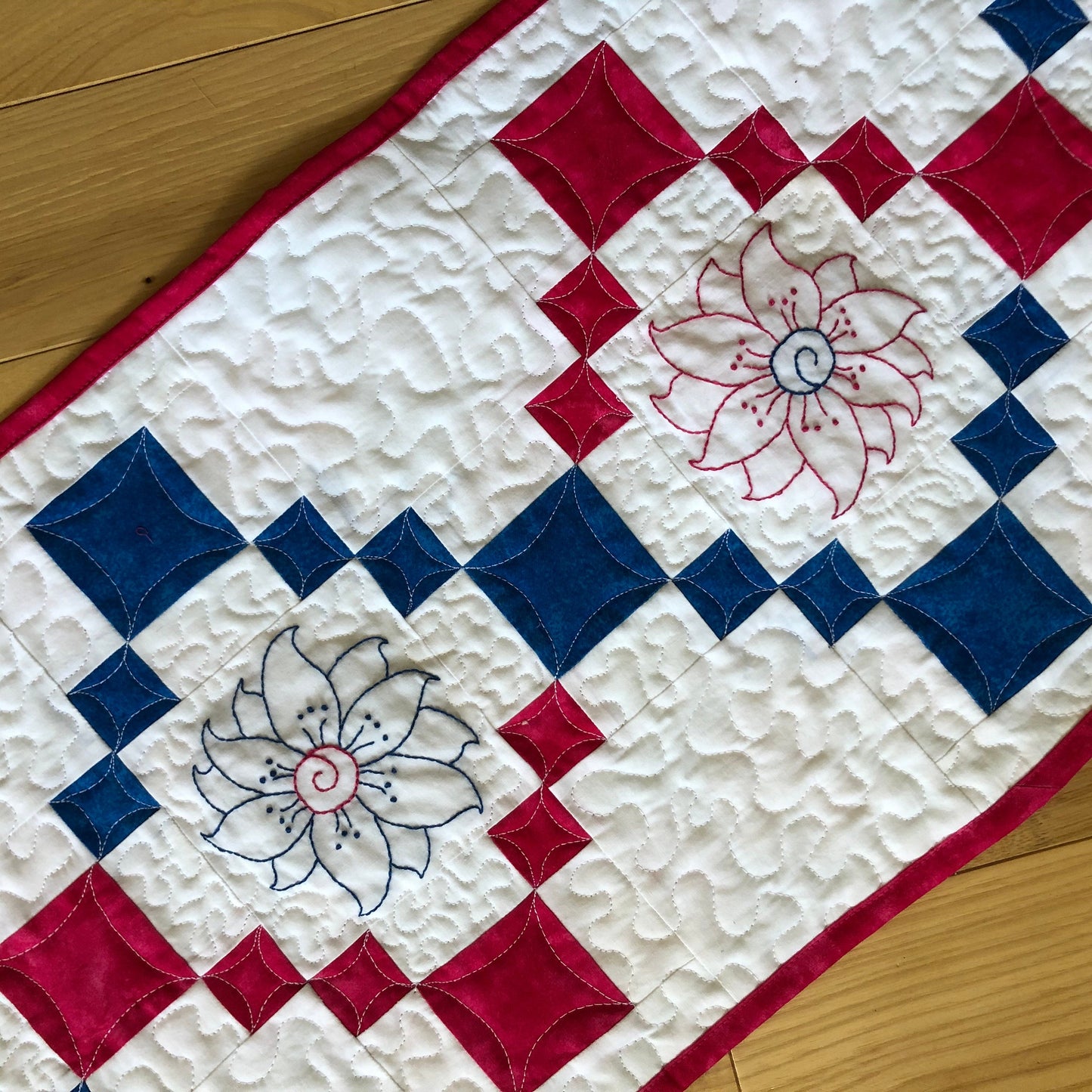 close up of flower embroidery and stippling quiltng on table runner.