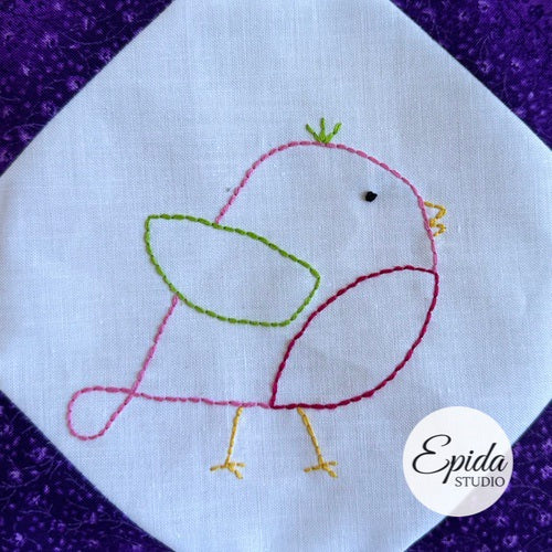 Embroidered bird design on a white fabric square with a purple border, featuring the Epida Studio logo.