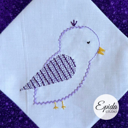 Embroidered bird design on a white fabric with purple border, featuring the Epida Studio logo.