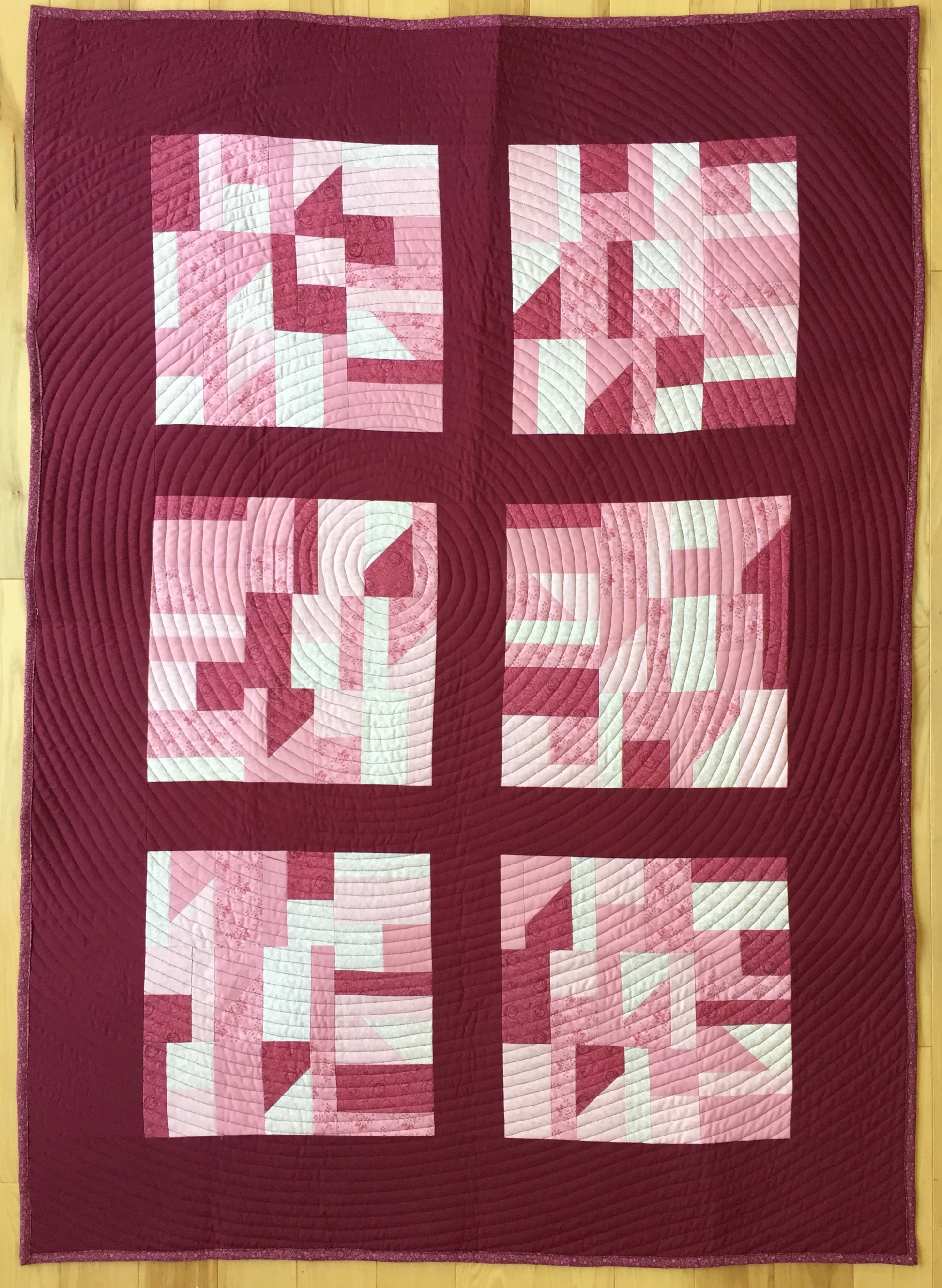 quilt with randomly pieced blocks in shades of pink with spiral quilting.
